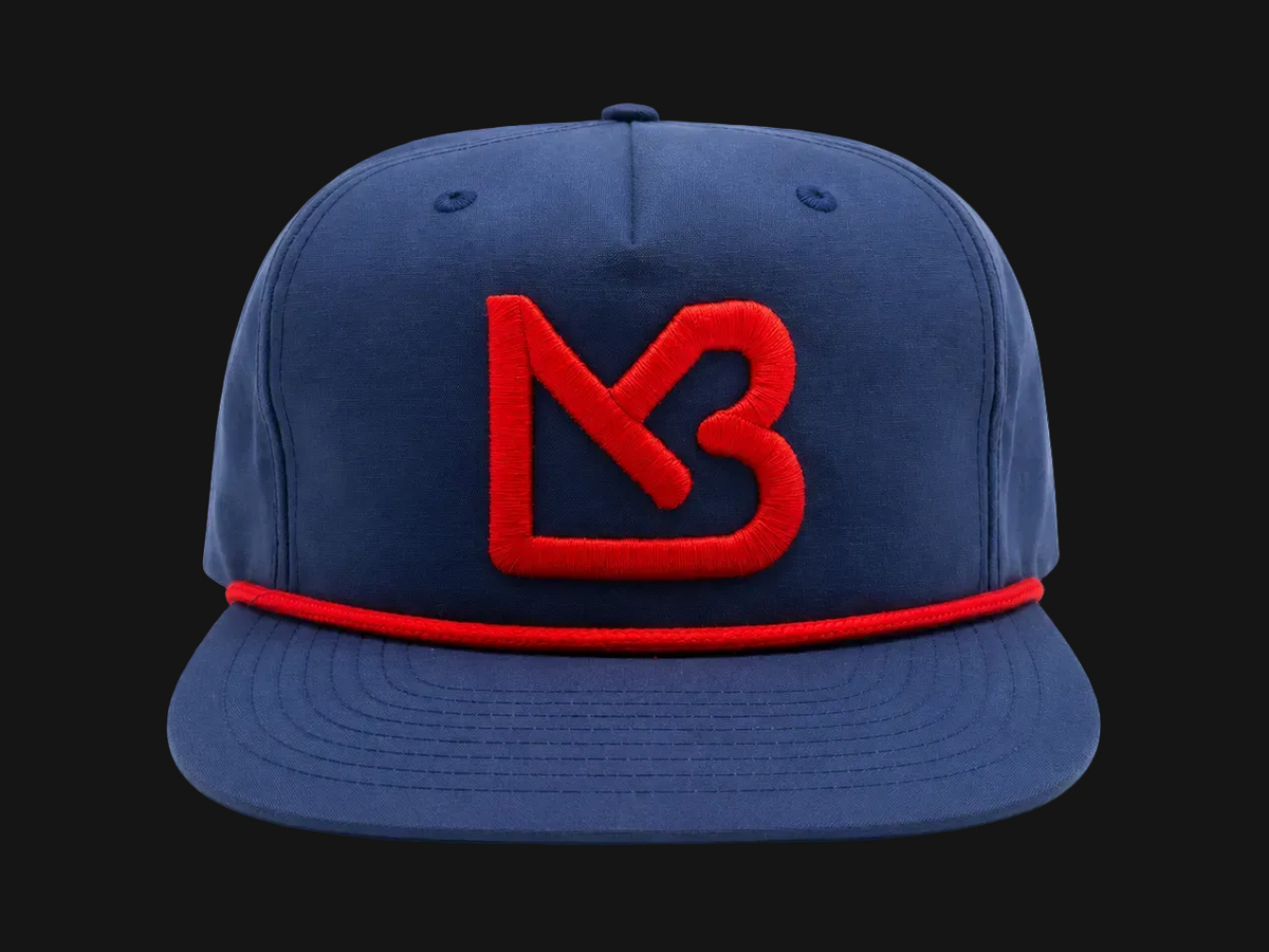 A navy blue flat-brim cap featuring a prominent red embroidered 'MB' logo on the front and a matching red embroidered band around the crown, set against a plain white background.