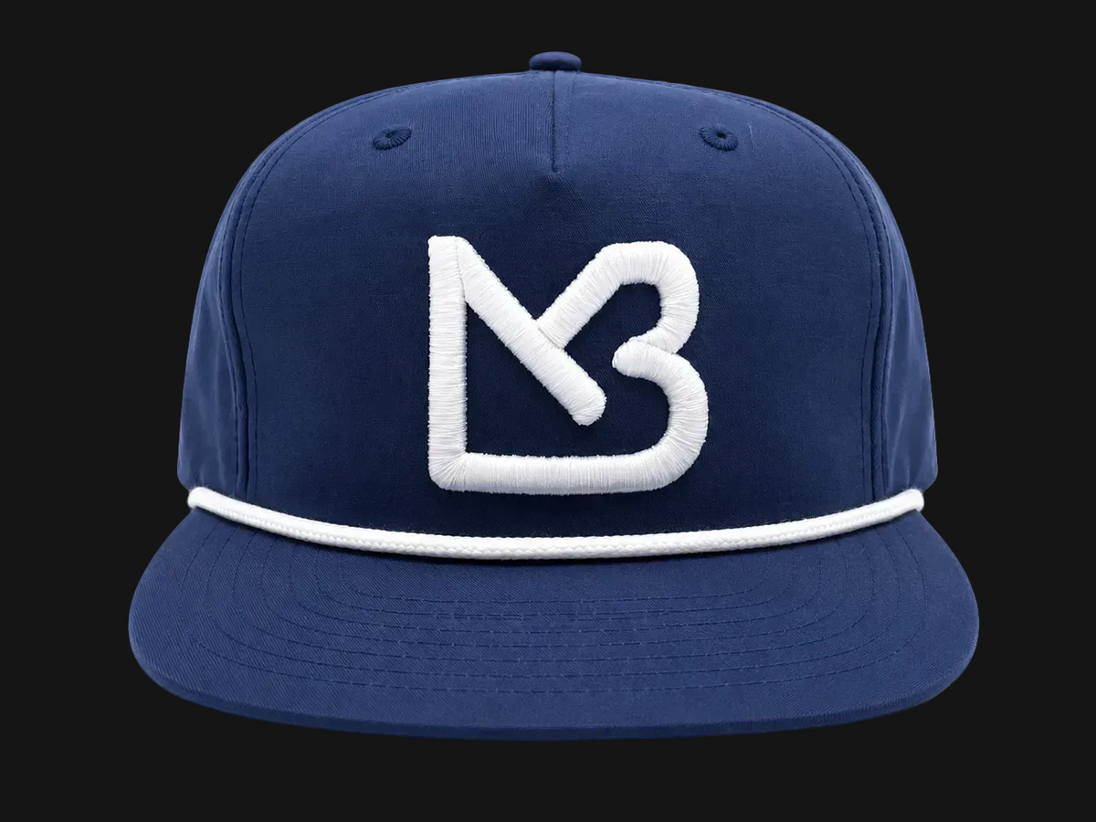 A navy blue flat-brim cap featuring a prominent white embroidered 'MB' logo on the front and a white stripe detail around the edge of the brim, shown against a plain white background.
